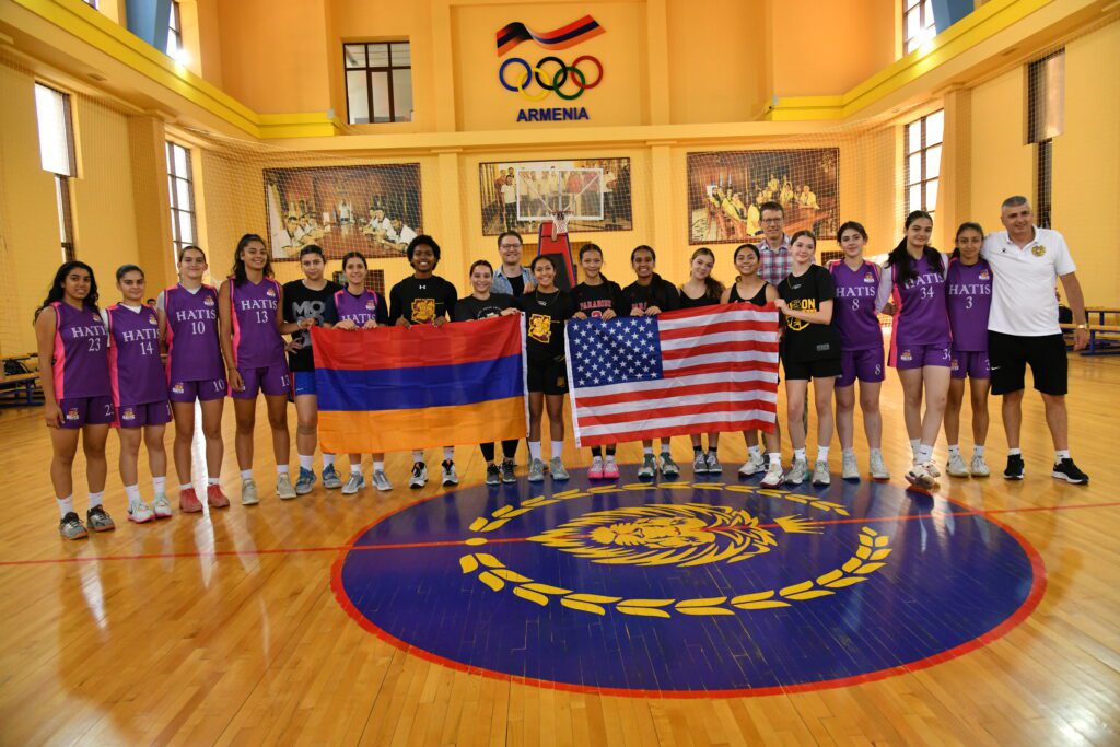 A group photo of U.S. girls basketball players and Armenia counterparts in a gym in Yerevan.