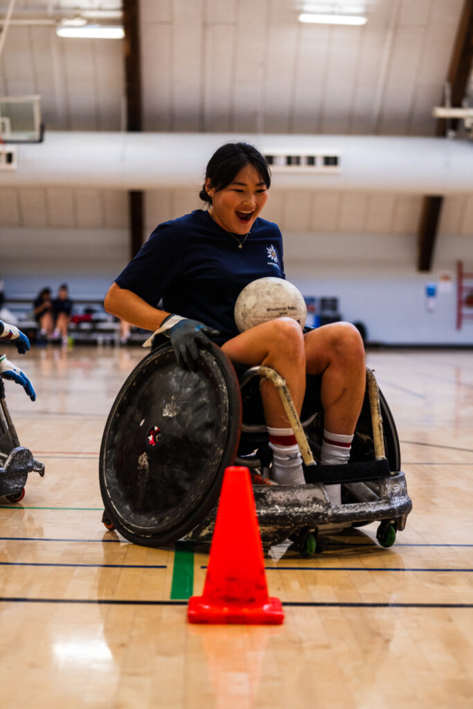 A female women's rugby player from Mongolia at the Northeast Passage wheelchair basketball practice. Smiling after scoring a point. 